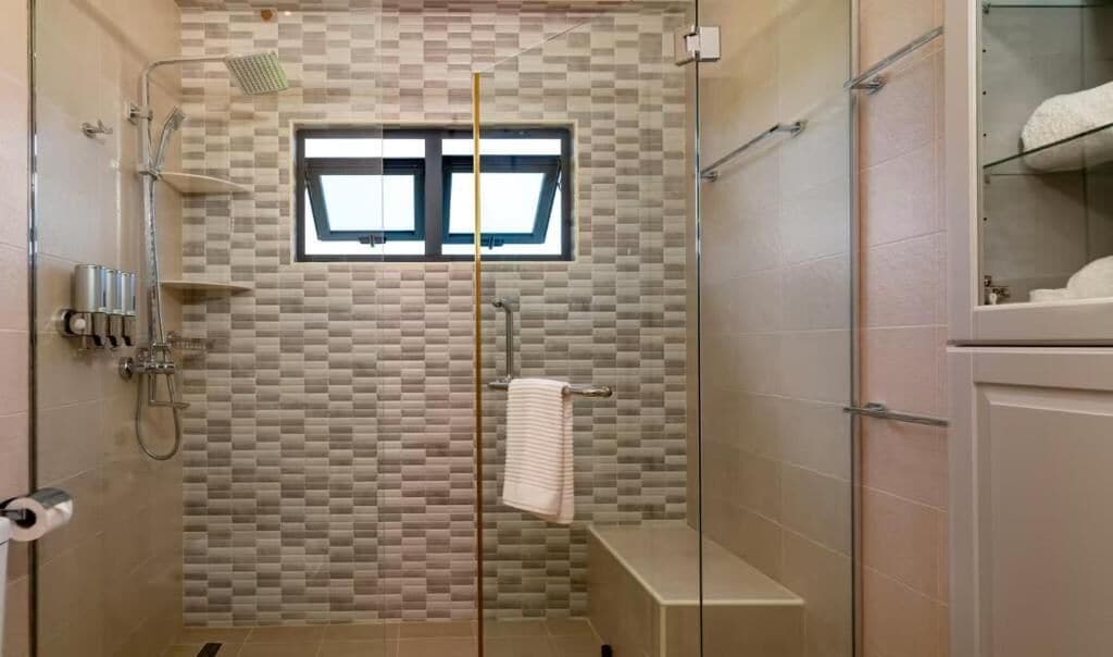 Eine Dusche mit Glastür, Handtuchhalter und einem Fenster darüber.