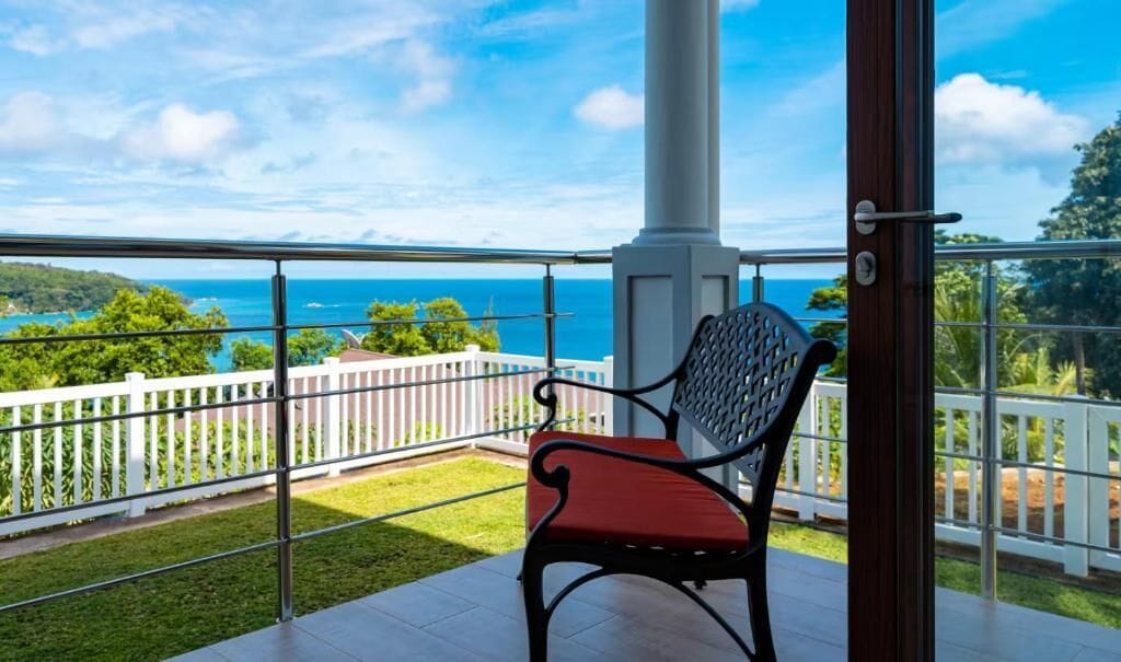 Ein Balkon mit Blick aufs Meer, ein weißer Zaun und ein roter Stuhl.