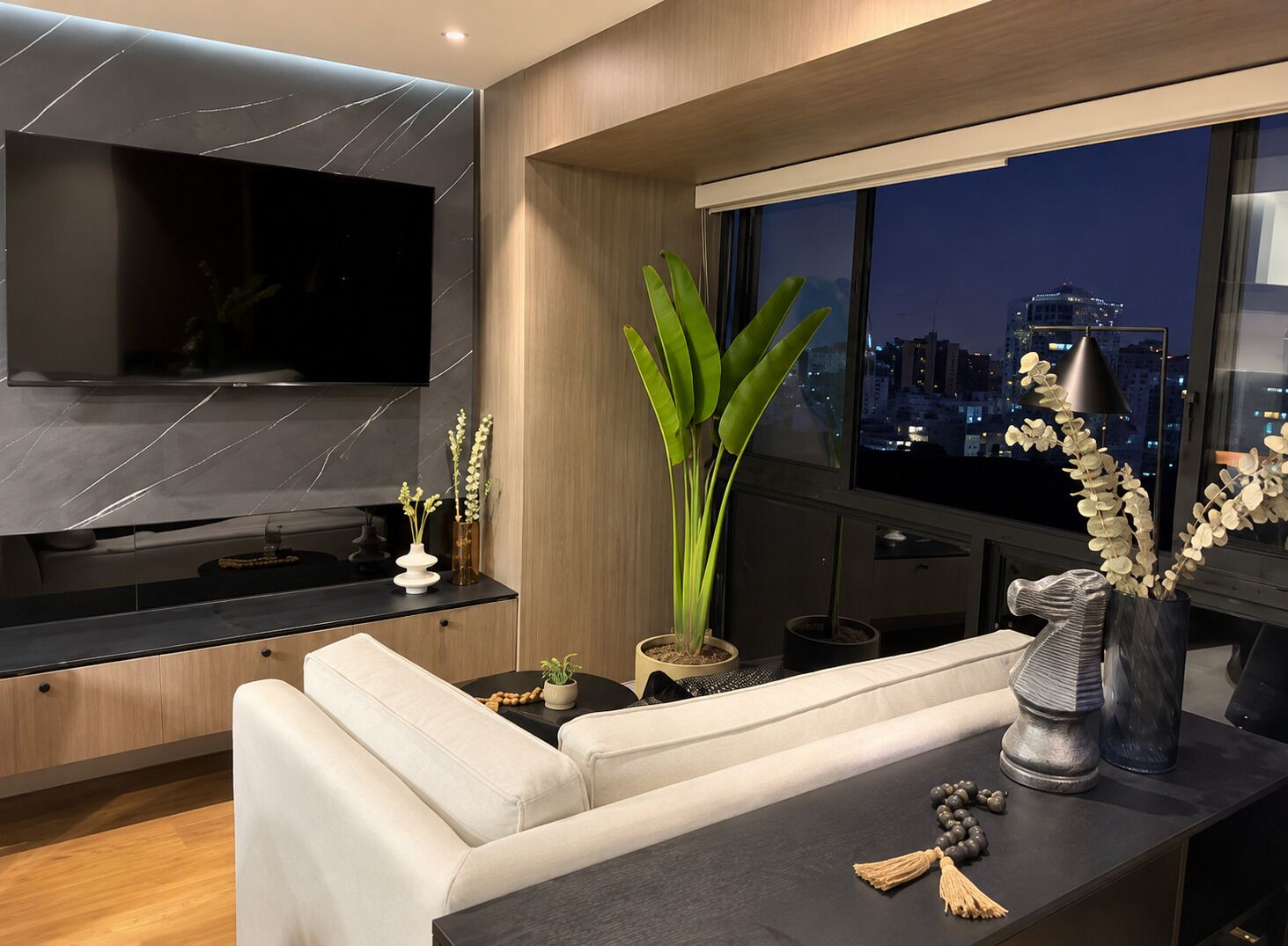 A modern living room with a sofa, a flat-screen TV, and a city view.