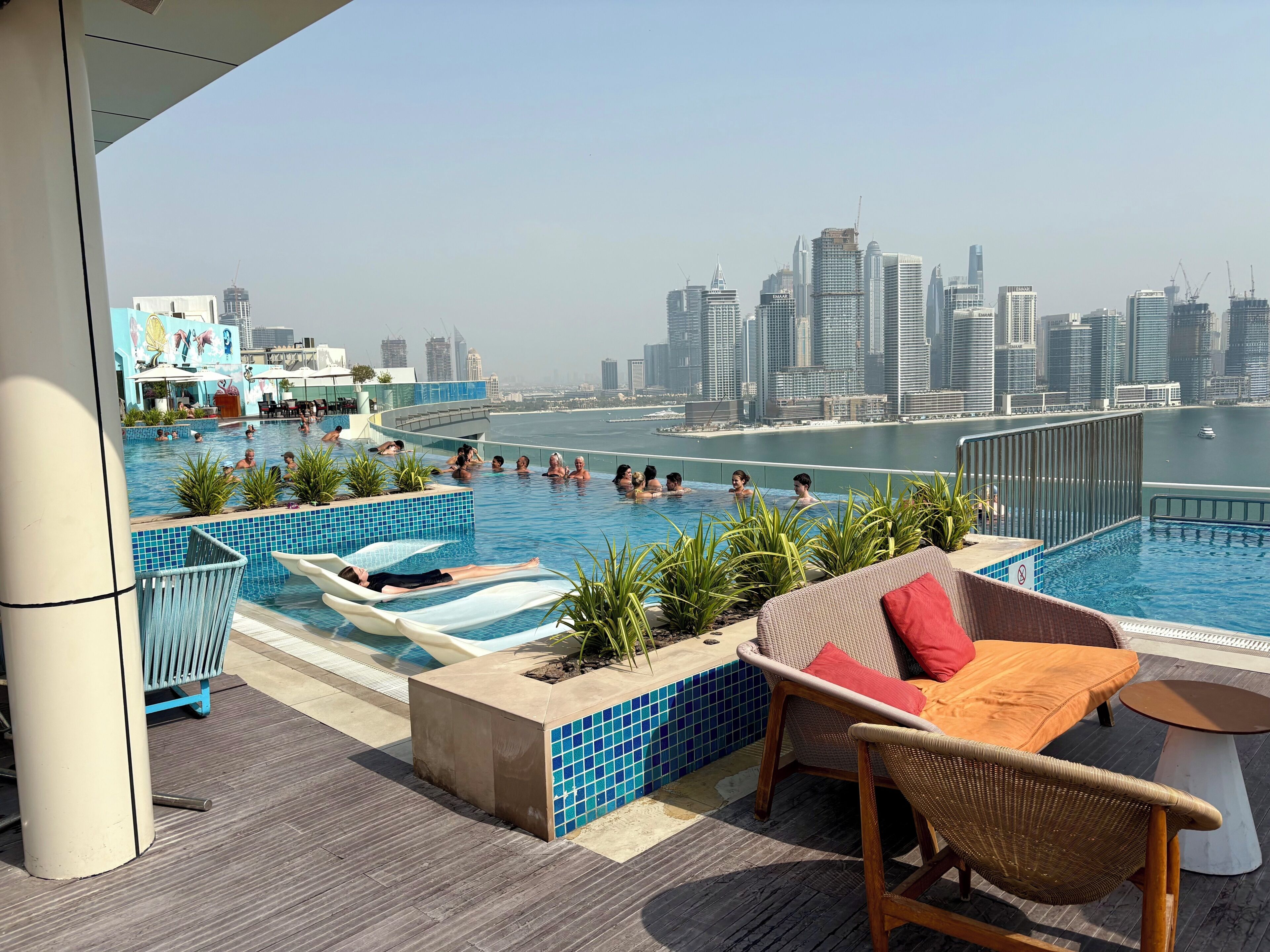 A rooftop pool area with a city skyline view, lounge chairs, and a poolside table.