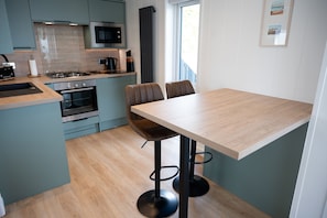A modern kitchen with a dining area, featuring a central island, built-in appliances, and a view of the outdoors. - Barlocco -  a lodge that sleeps 2 guests  in 1 bedroom (Isles of Fleet Retreat, Gatehouse of Fleet)