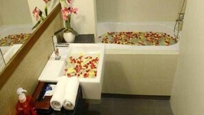 A bathroom with a bathtub filled with rose petals, a sink with a flower arrangement, and a mirror.