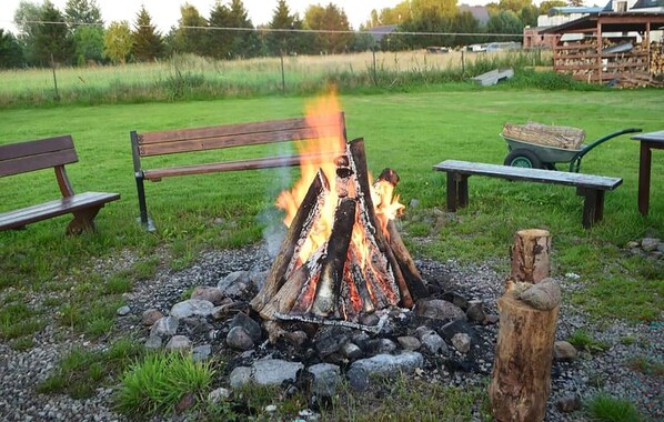 A campfire with benches and a wheelbarrow in a grassy field.