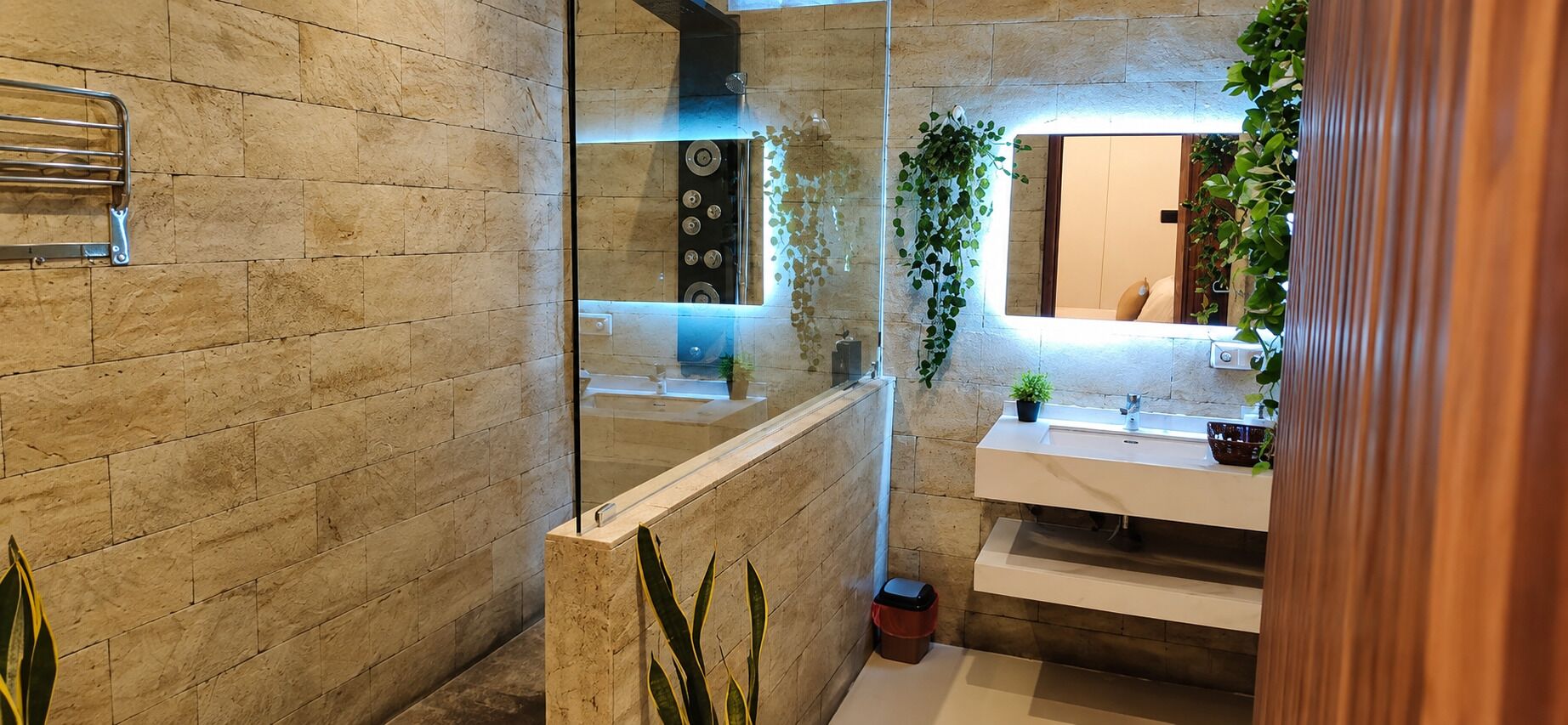 A bathroom with a stone wall, a glass shower enclosure, a sink with a mirror, and a potted plant.