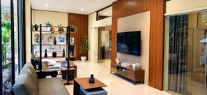 Una sala de estar moderna con sofá, mesa de centro y televisor montado en la pared. Se observa una estantería con objetos decorativos y una planta en maceta.