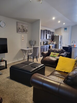 Ein modernes Wohnzimmer mit Ledersofa, Flachbildfernseher und Essbereich mit Tisch und Stühlen.
