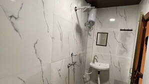 Un baño con paredes de mármol blanco, ducha, lavabo e inodoro.