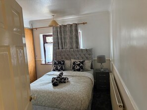Ein Schlafzimmer mit einem Bett, einem Nachttisch, einer Lampe und einem Fenster mit Vorhängen.