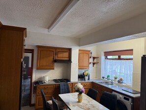 A kitchen with wooden cabinets, a stove, a sink, and a dining table with chairs. - Fully Furnished Double Bedroom – Excellent Location to city centre. (Coventry)