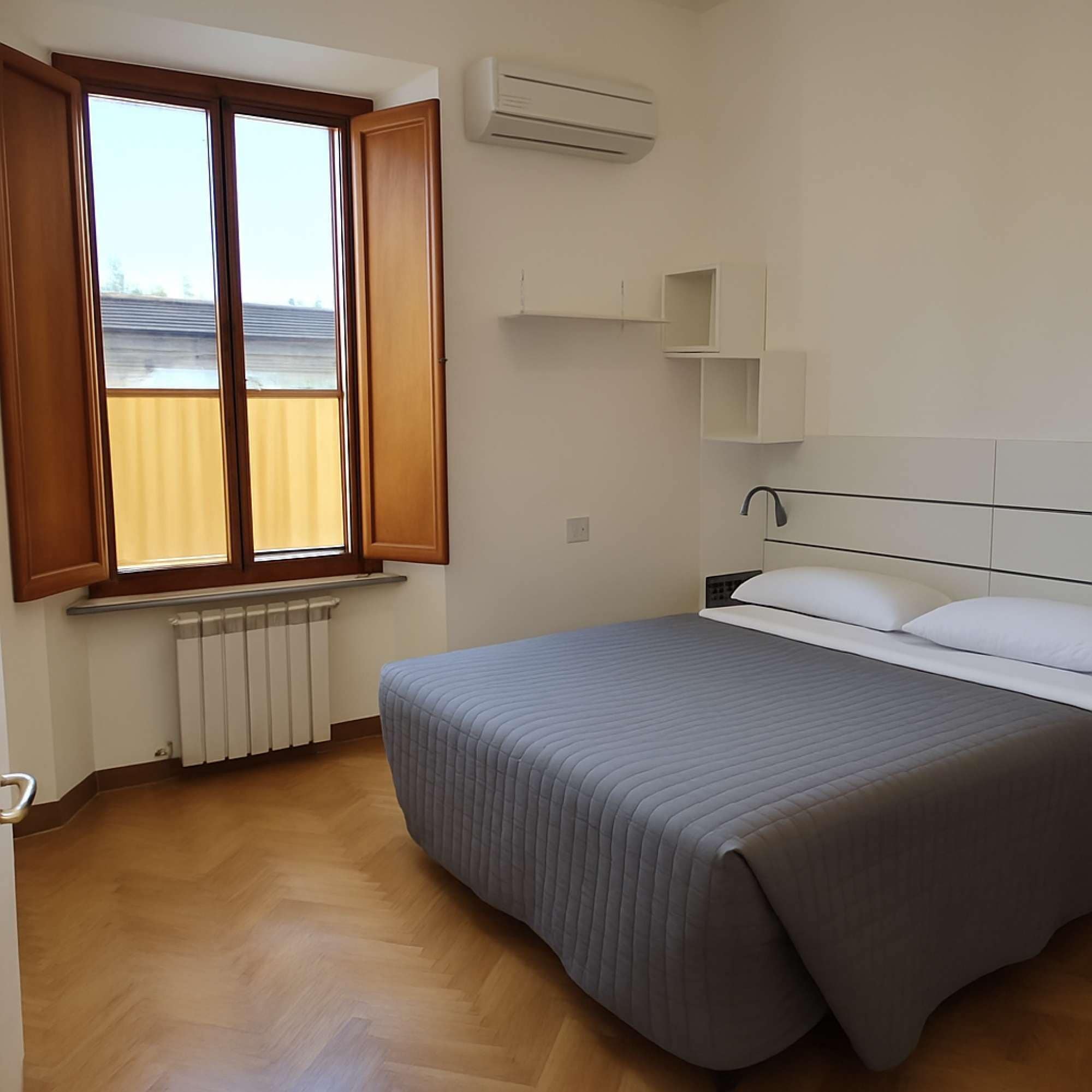 Ein Schlafzimmer mit Bett, einem Fenster mit Holzjalousien, einem Heizkörper und einer Wand-Klimaanlage.