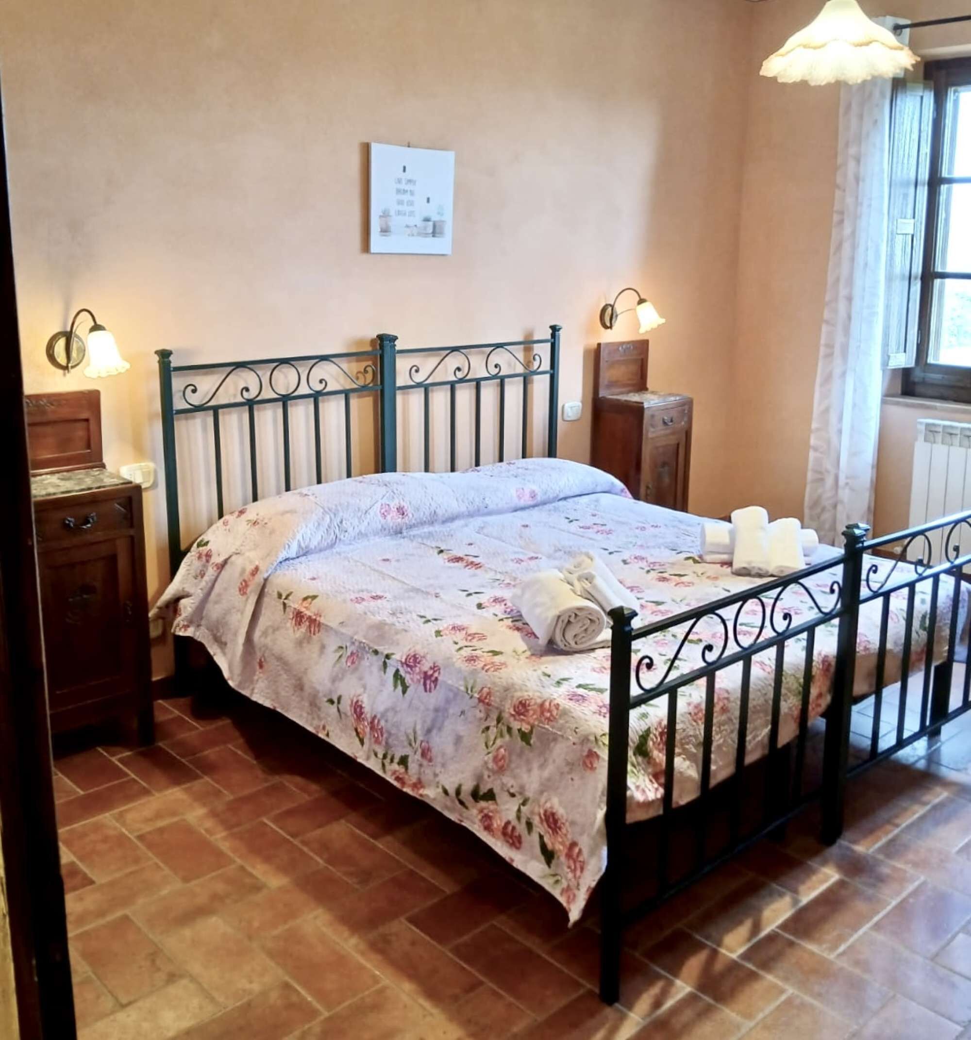 Une chambre à coucher avec un lit, une table de chevet, une lampe fixée au mur et une fenêtre avec des rideaux.