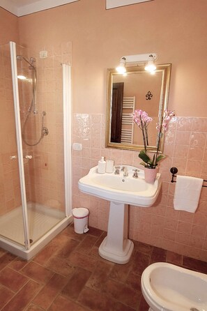 A bathroom with a glass shower enclosure, a pedestal sink, a mirror with lights, and a toilet. - Apartment in Piazza del Campo area 3 bedrooms 2 bathrooms (Asciano)