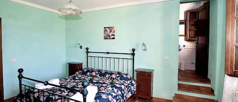 A bedroom with a bed, a nightstand, a wall-mounted light, a small picture, and a staircase leading to another room.