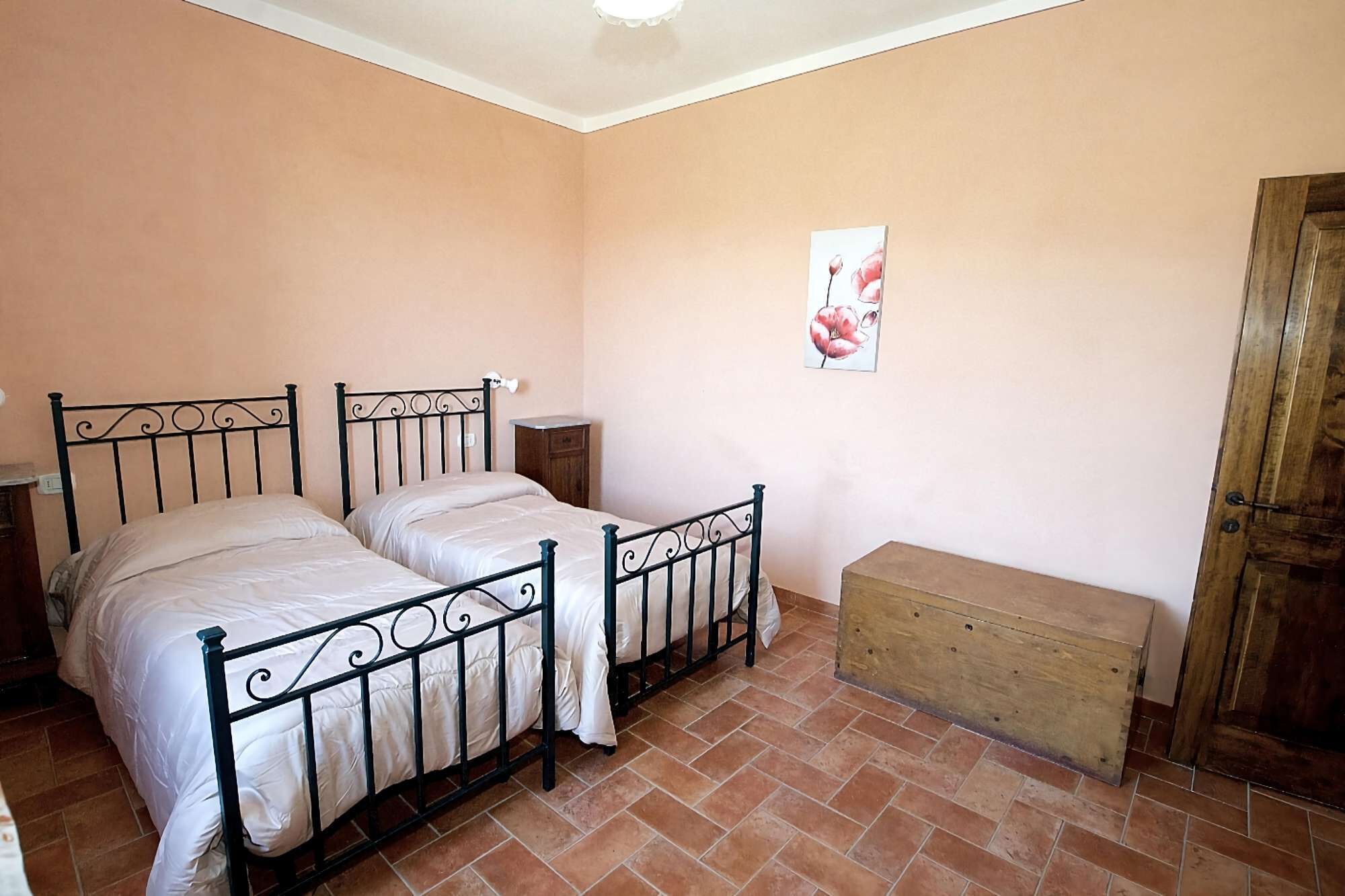 Un dormitori amb dos llits, una banca de fusta, una porta de fusta i un quadre penjat a la paret.