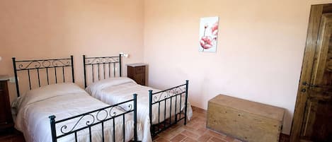 A bedroom with two beds, a wooden bench, a wooden door, and a wall-mounted picture.