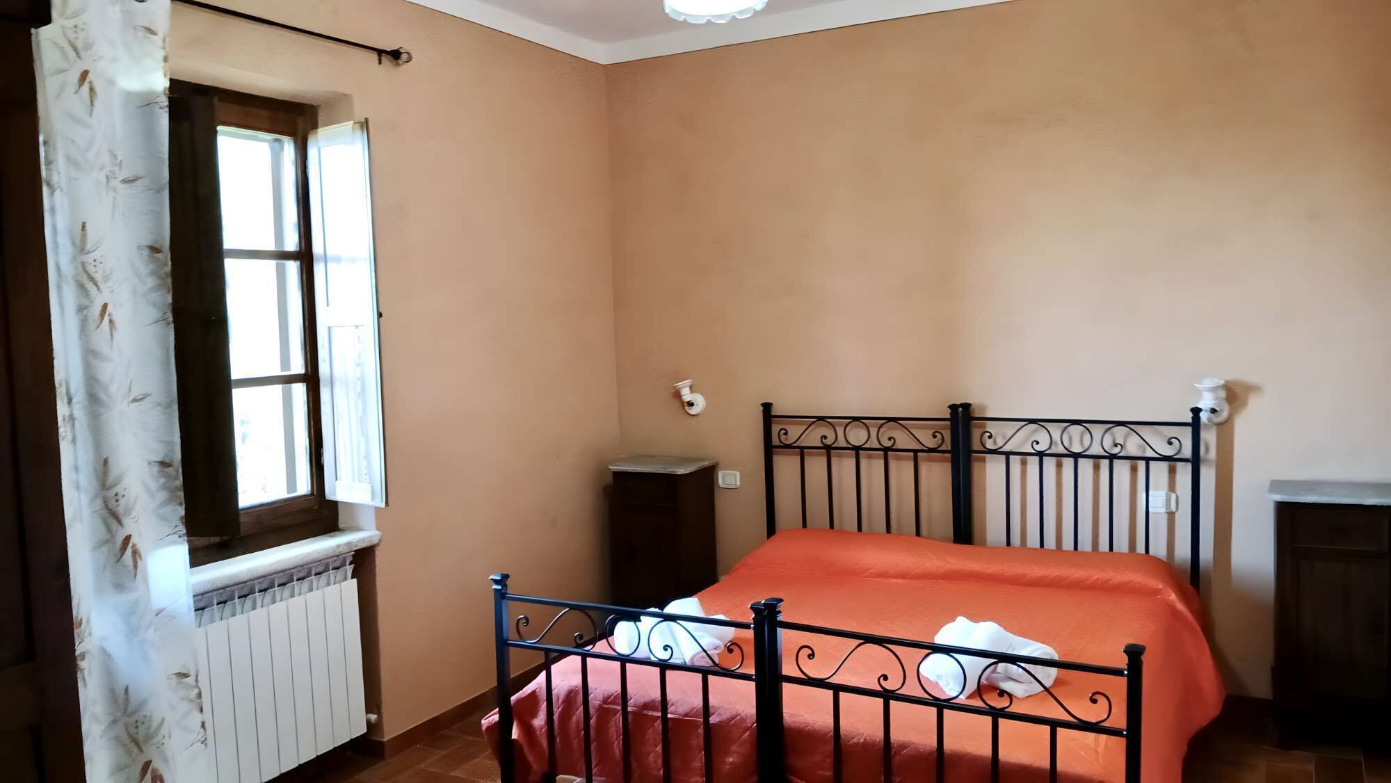 A bedroom with a bed, a radiator, a window, and a small cabinet.