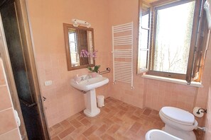 A bathroom with a white sink, a mirror, a toilet, and a window with a view of trees. - Apartment in Piazza del Campo area 3 bedrooms 2 bathrooms (Asciano)