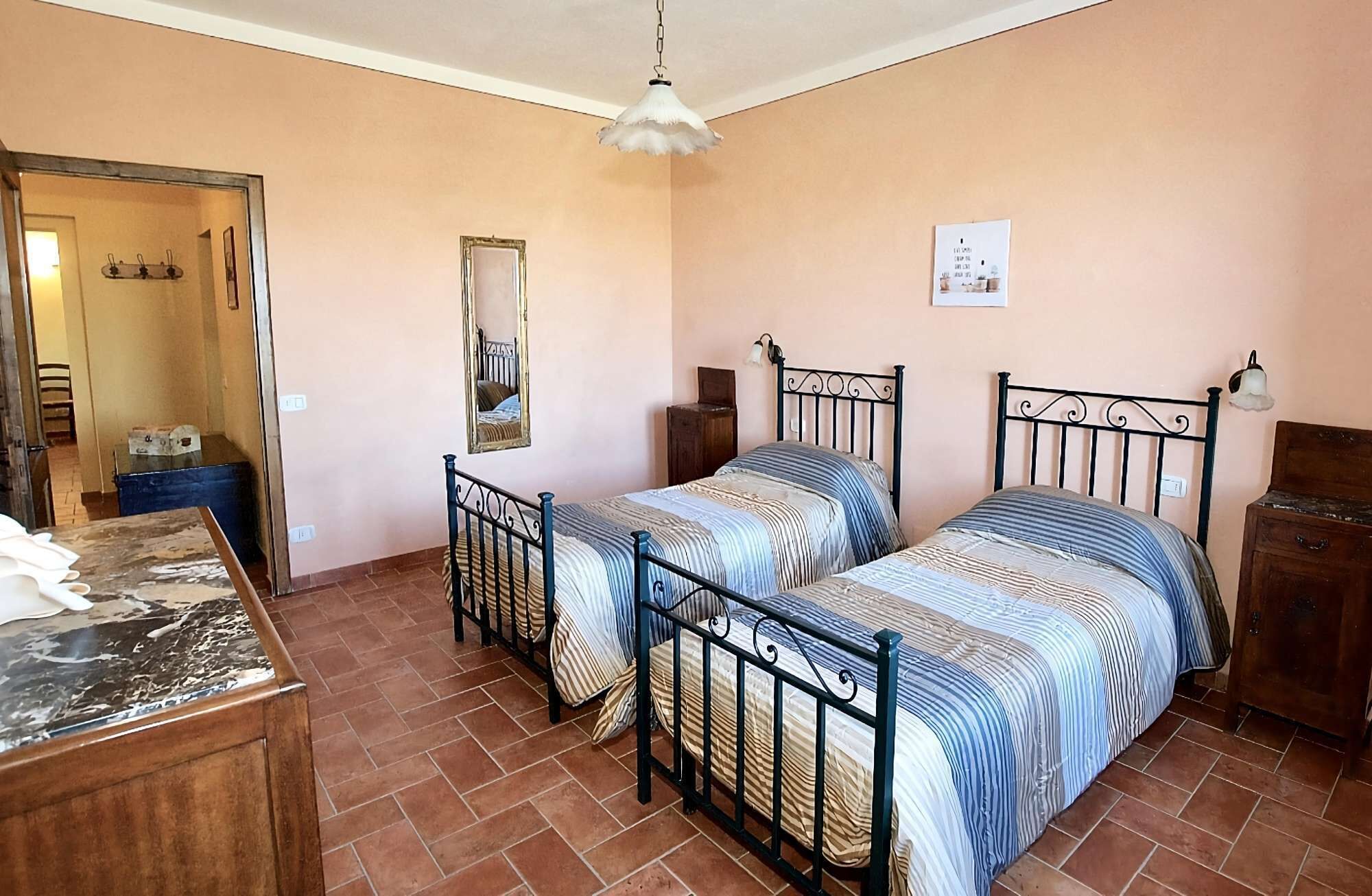 A bedroom with two beds, a wooden dresser, a mirror, and a hanging light fixture.