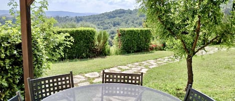 Un patio al aire libre con una mesa redonda y sillas, rodeado de follaje y un camino de piedra.