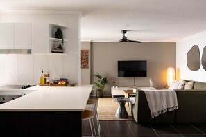 Eine moderne Küche mit einer zentralen Kochinsel, einem Essbereich mit einer Couch und einem an der Wand montierten Flachbildfernseher.
