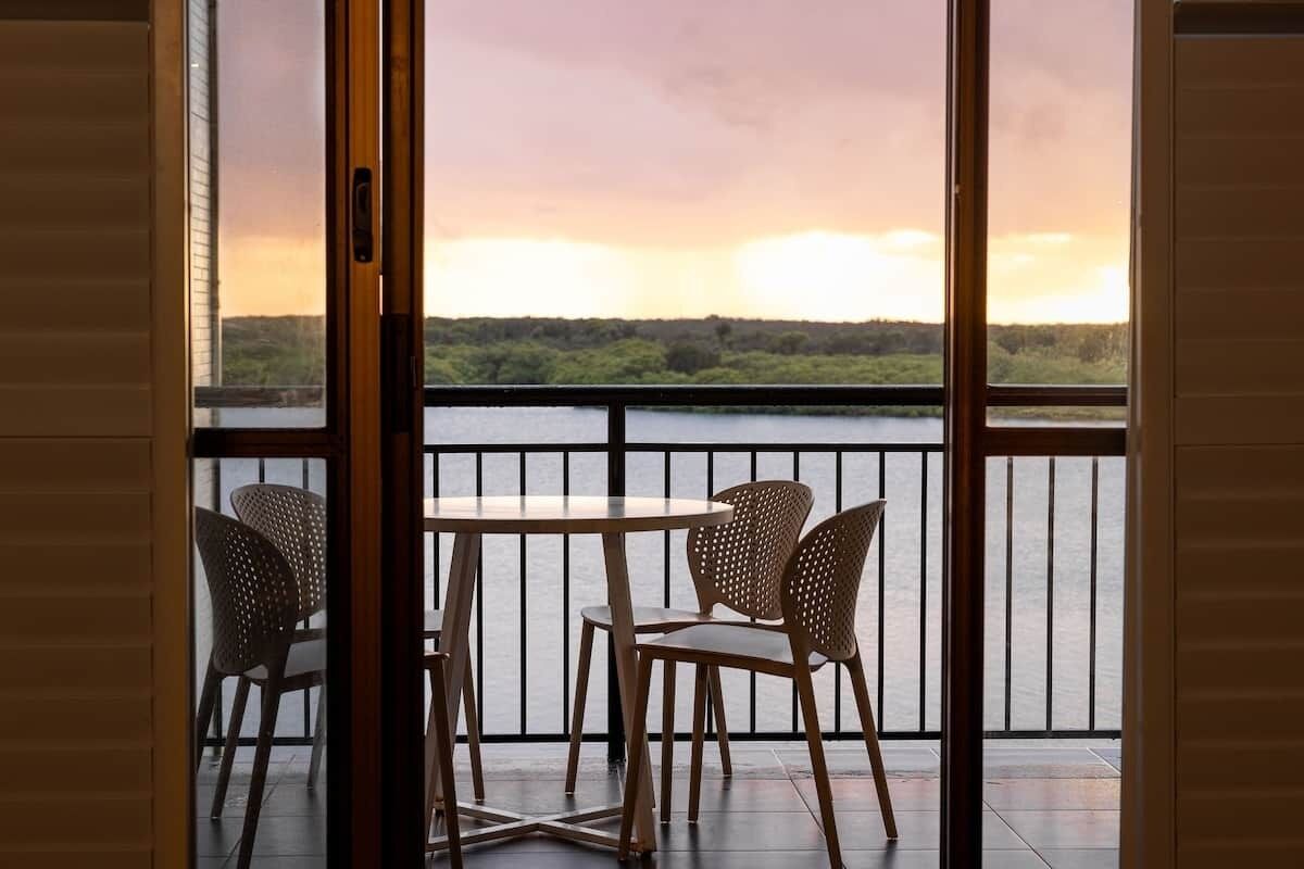 Ein Balkon mit Tisch und Stühlen, der auf ein Gewässer und eine grüne Landschaft blickt.