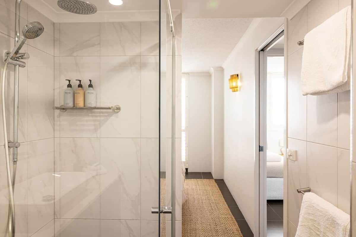 A modern bathroom with a glass shower enclosure, a towel rack, and a shelf with toiletries.