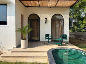 Una casa con un porche cubierto, dos puertas arqueadas, una piscina pequeña y dos sillas.