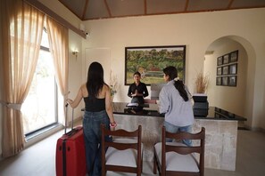 Una recepción con una recepcionista, una ventana con cortinas y un cuadro en la pared.