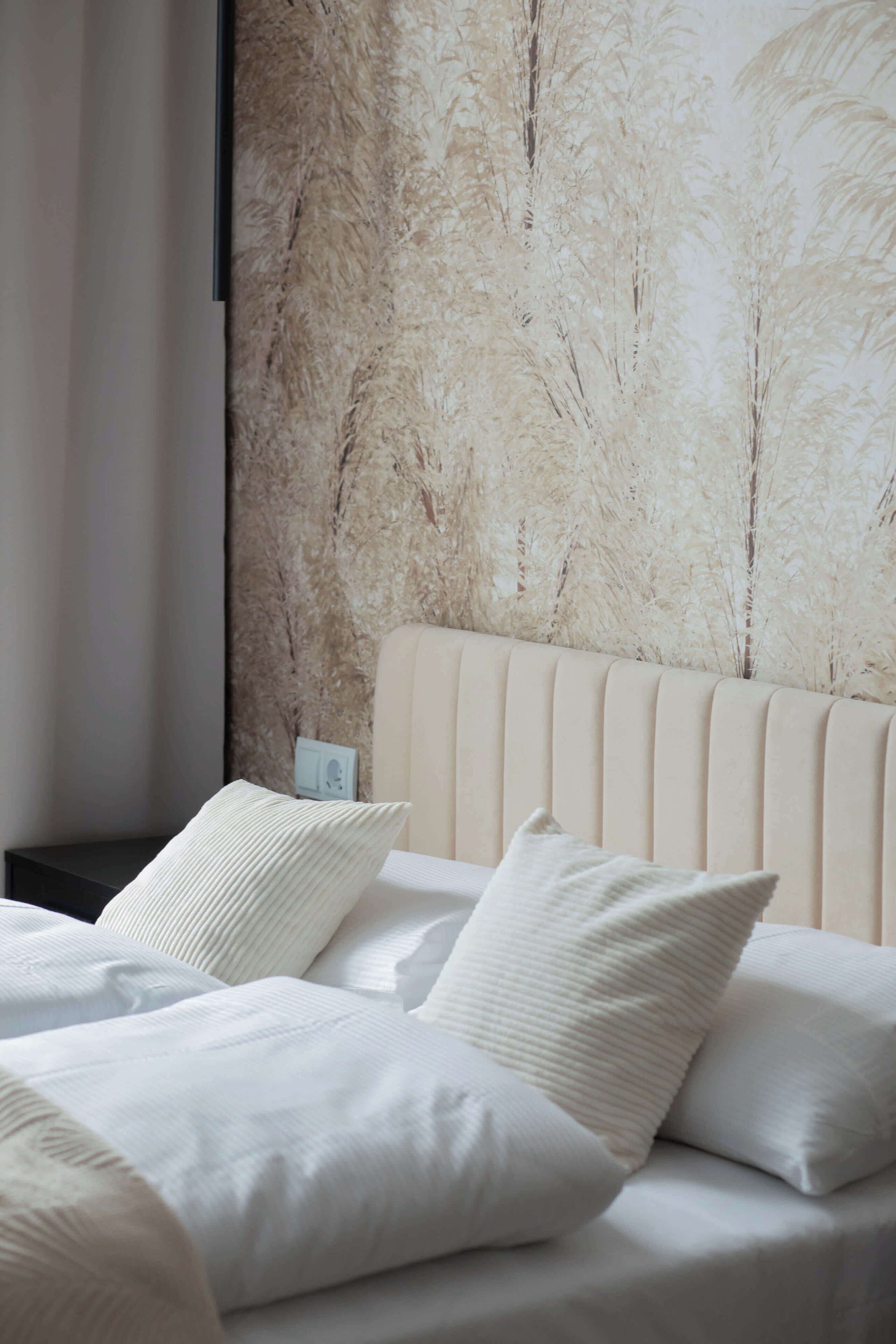 Une chambre à coucher avec un lit, des oreillers, une table de chevet et un mur orné d’un motif texturé.