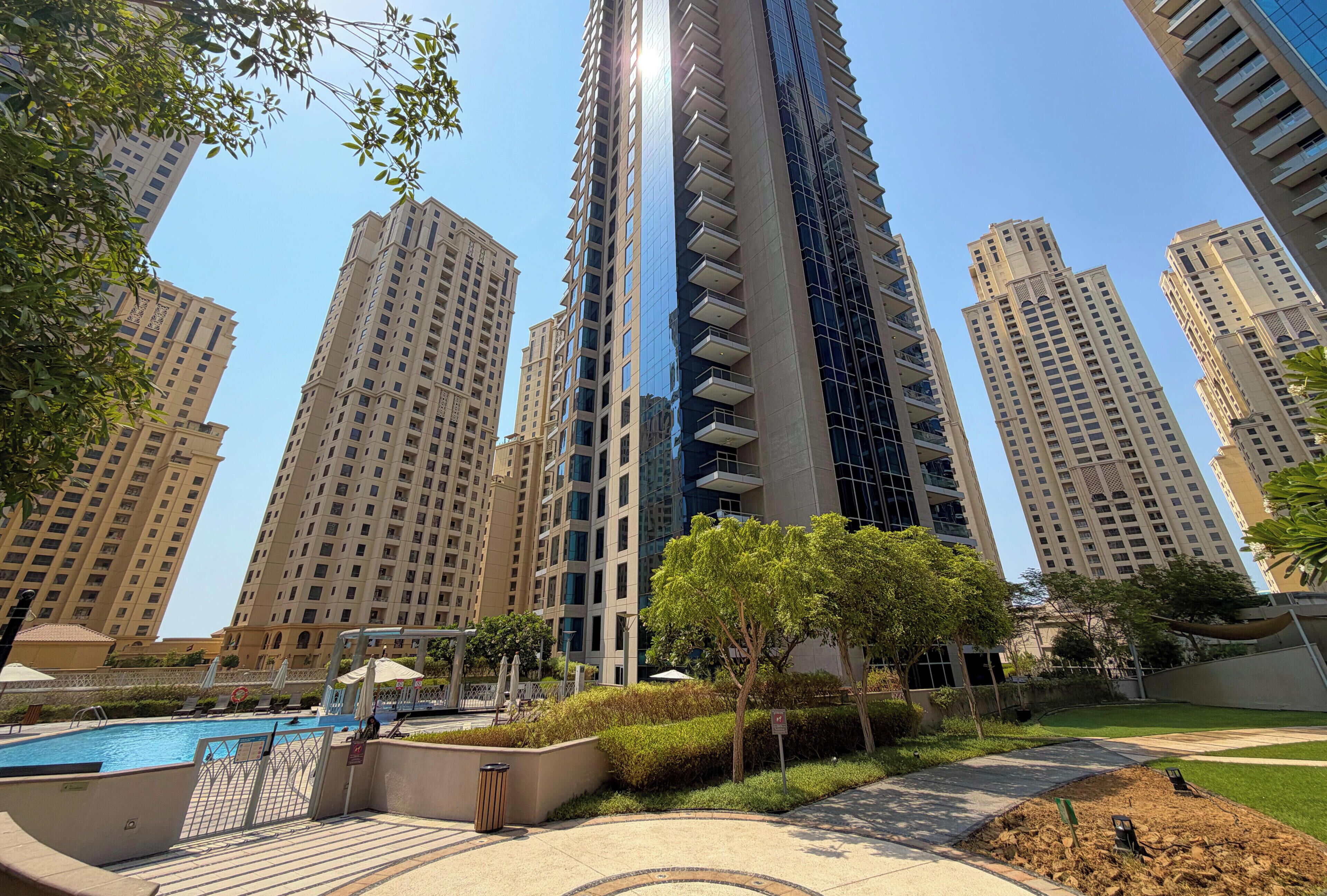 A high-rise residential building with a swimming pool and landscaped garden.