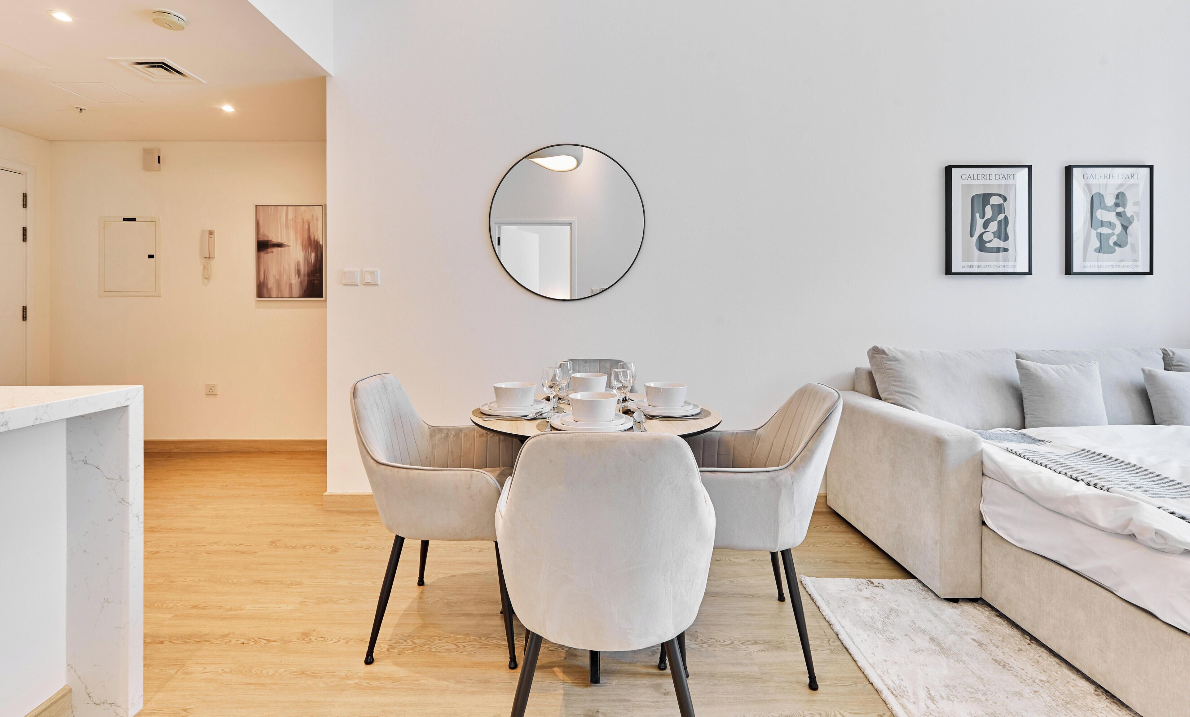 A modern living room with a dining area, a round mirror, and two framed artworks on the wall.