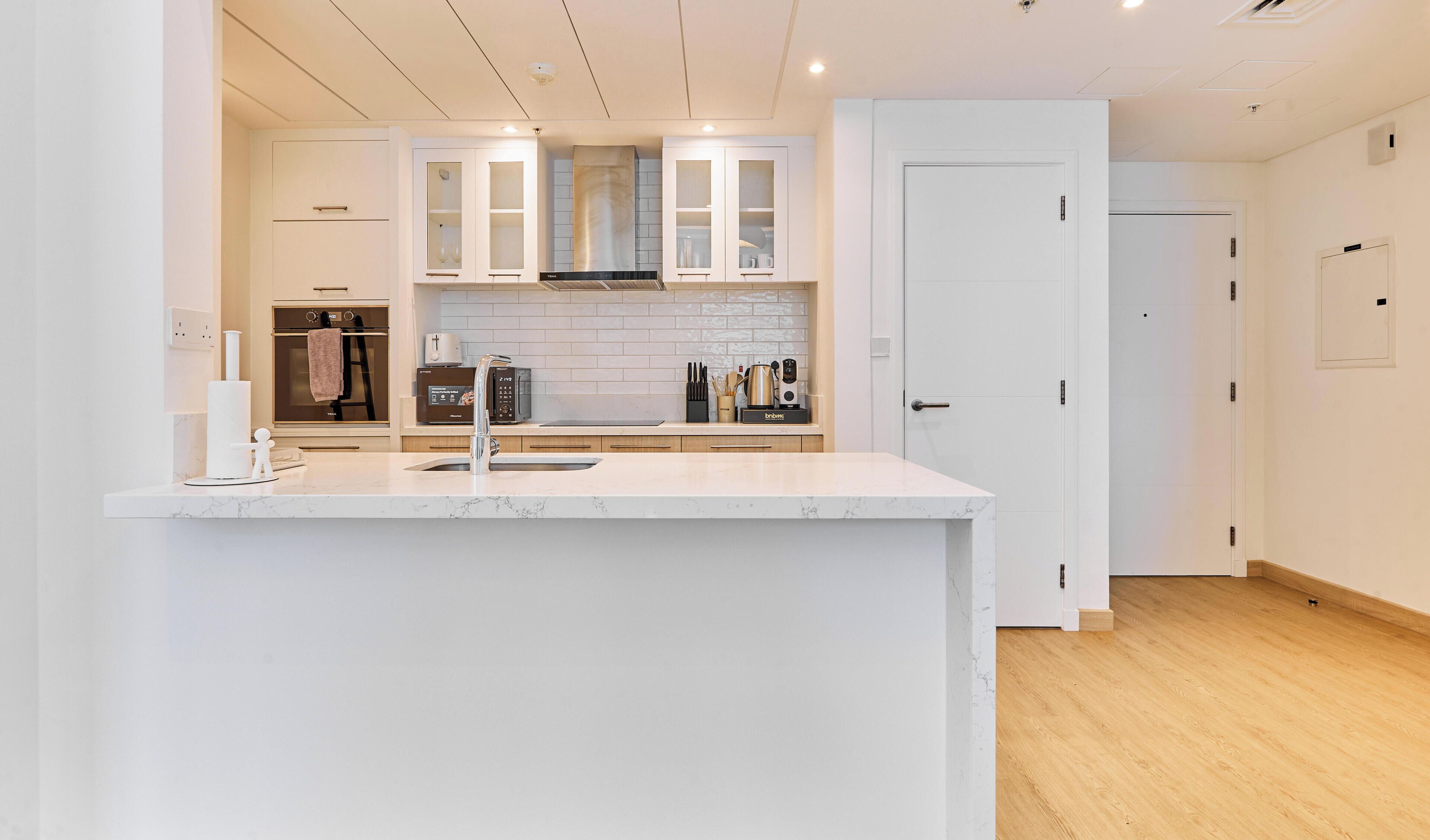 A modern kitchen with a marble countertop, built-in appliances, and a white door.