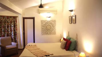A hotel room with a bed, a chair, a decorative wall piece, and a wall-mounted air conditioner.