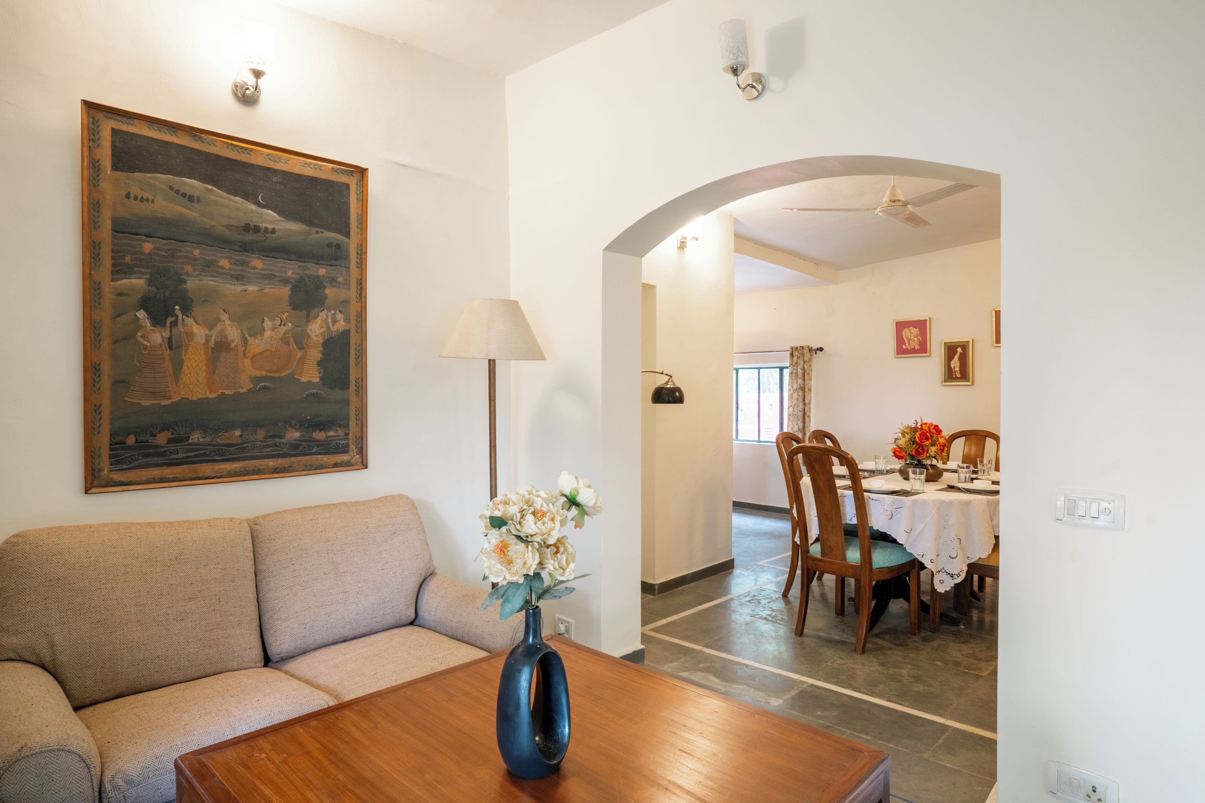 Sala de estar com sofá, mesa com vaso, quadro e canto de jantar com cadeiras e mesa.