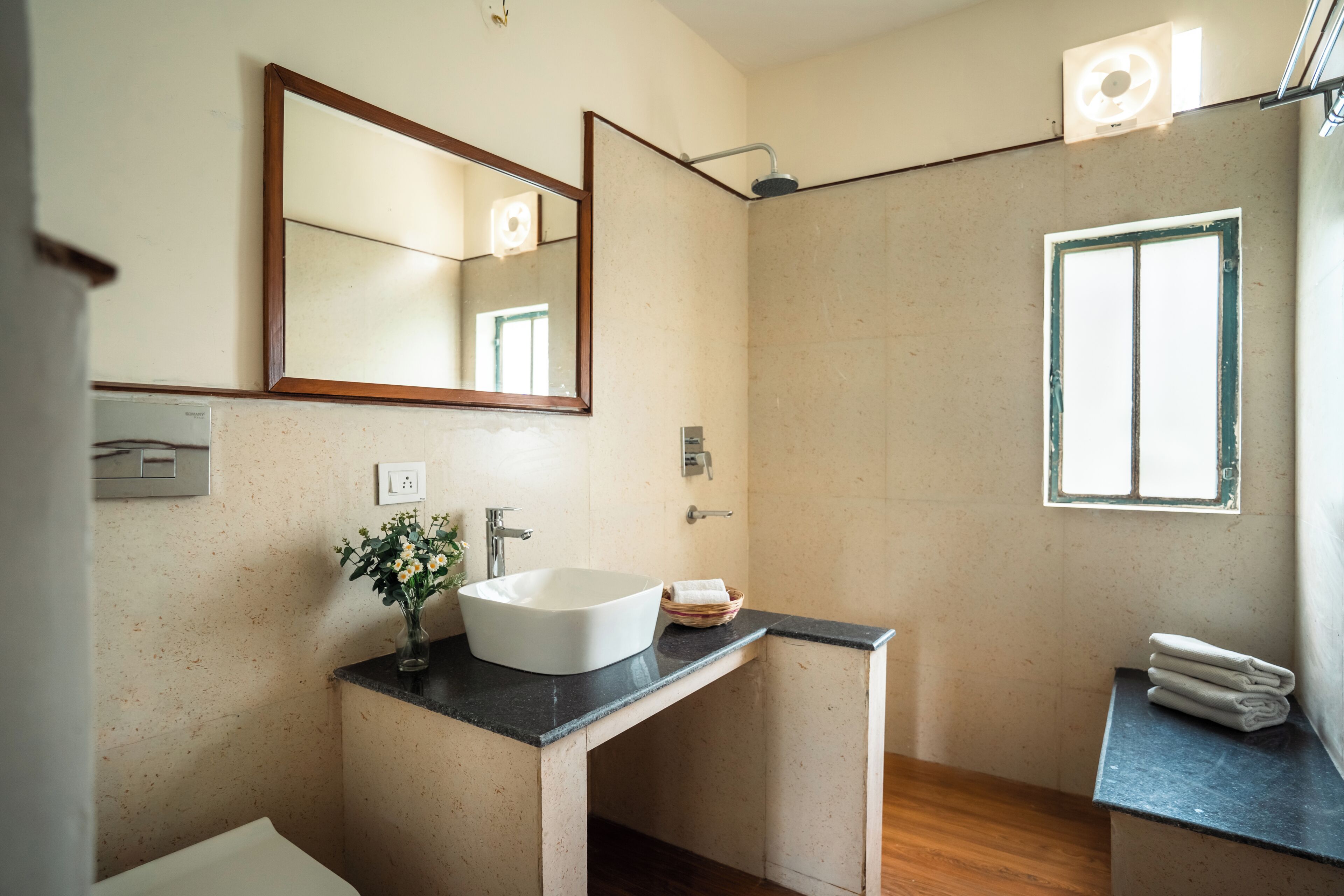 A modern bathroom with a freestanding sink, a mirror, a shower, and a window.