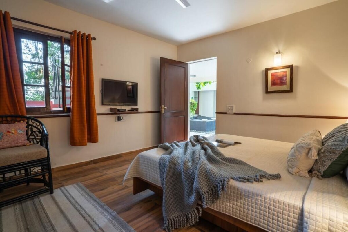 Un dormitori amb un llit, una televisió, una porta que dóna a l'exterior i una finestra amb cortines.