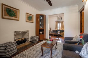 Una sala de estar con chimenea, sofá, reposapiés y una mesa con frutero.