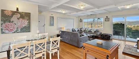 A spacious living area with a dining table, chairs, sofas, and a view through large windows.