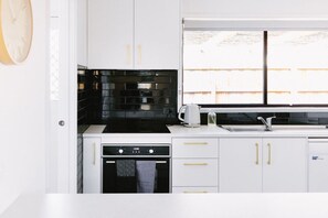 A modern kitchen with white cabinetry, a black backsplash, and a window with a view of a fence.