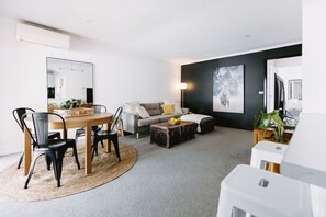 A modern living room with a dining area, a grey sofa, a coffee table, and a large framed picture on the wall.