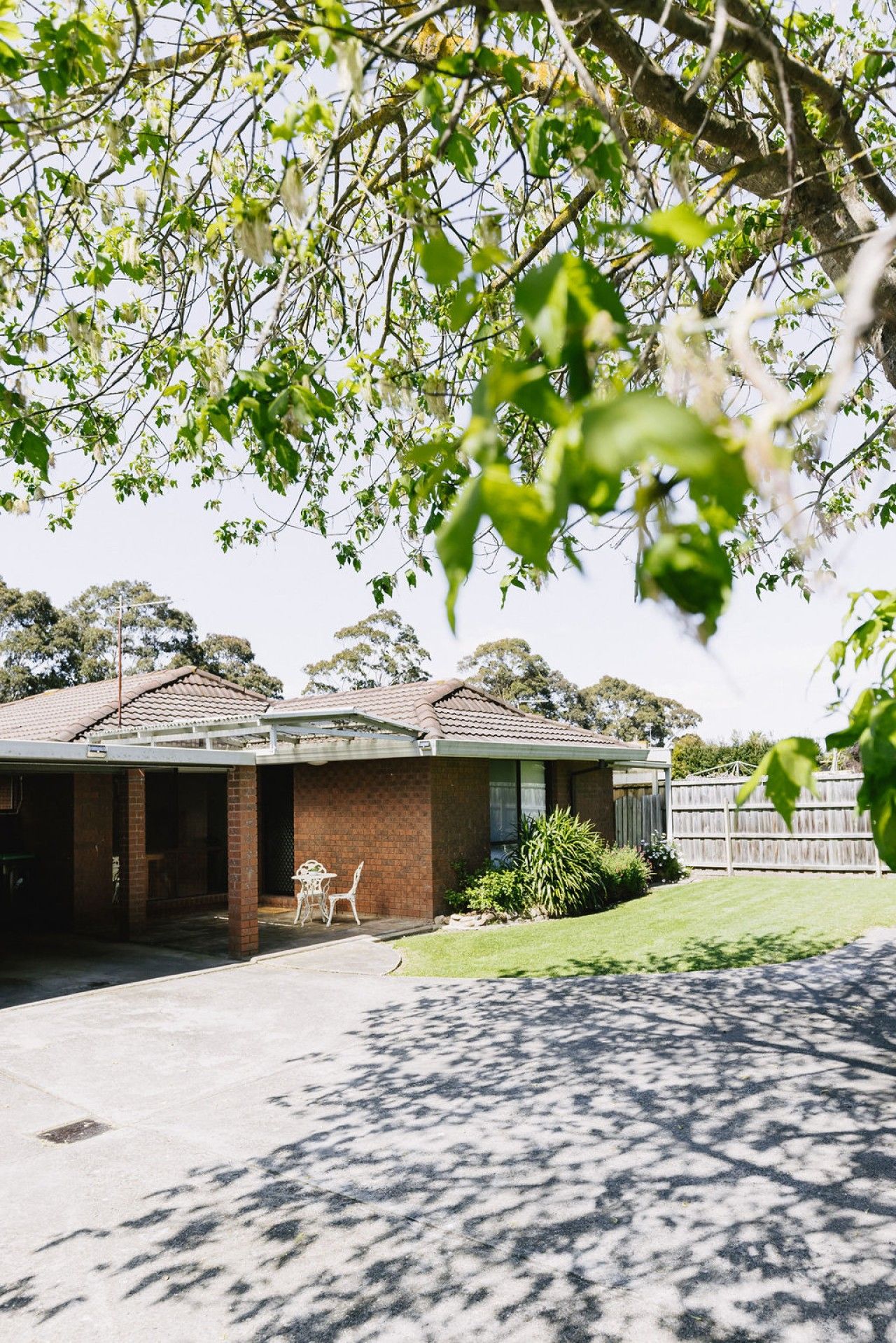 A residential property with a brick house, a covered outdoor seating area, and a well-maintained lawn.