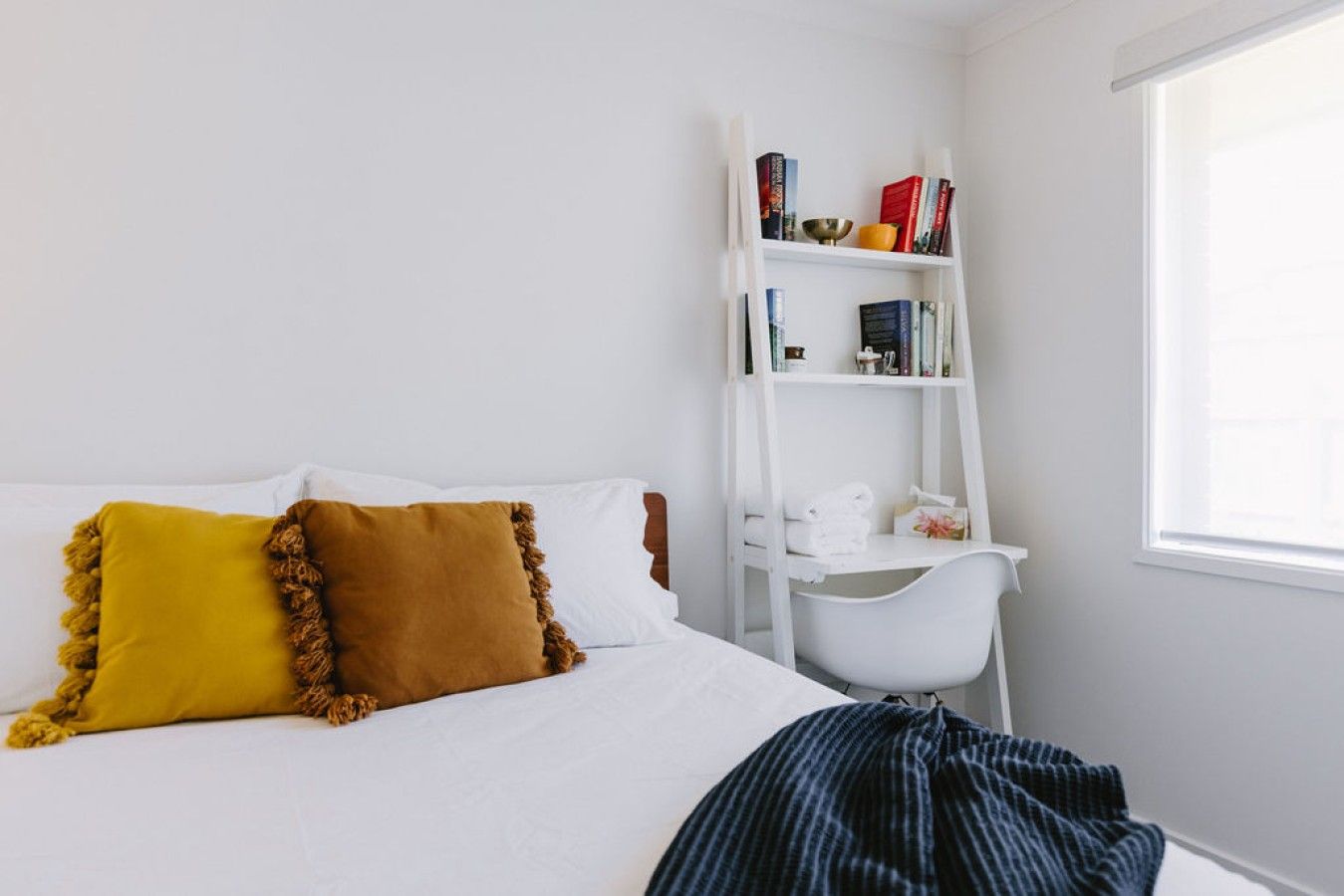 A bedroom with a bed, a white bookshelf, and a window.