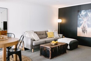 A modern living room with a grey sofa, a wooden dining table, and a vintage trunk.