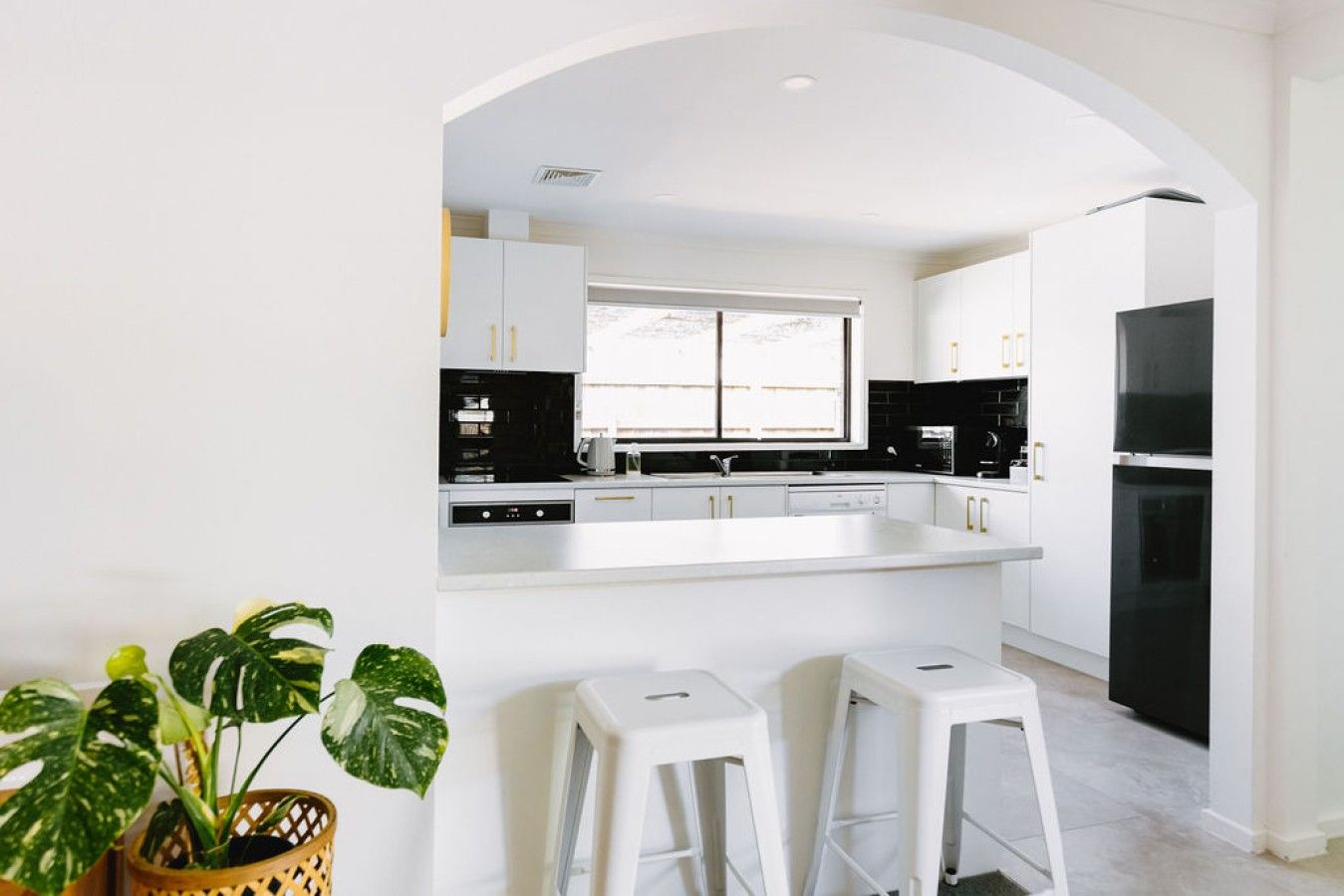 A modern kitchen with white cabinetry, a black refrigerator, and a window providing natural light.