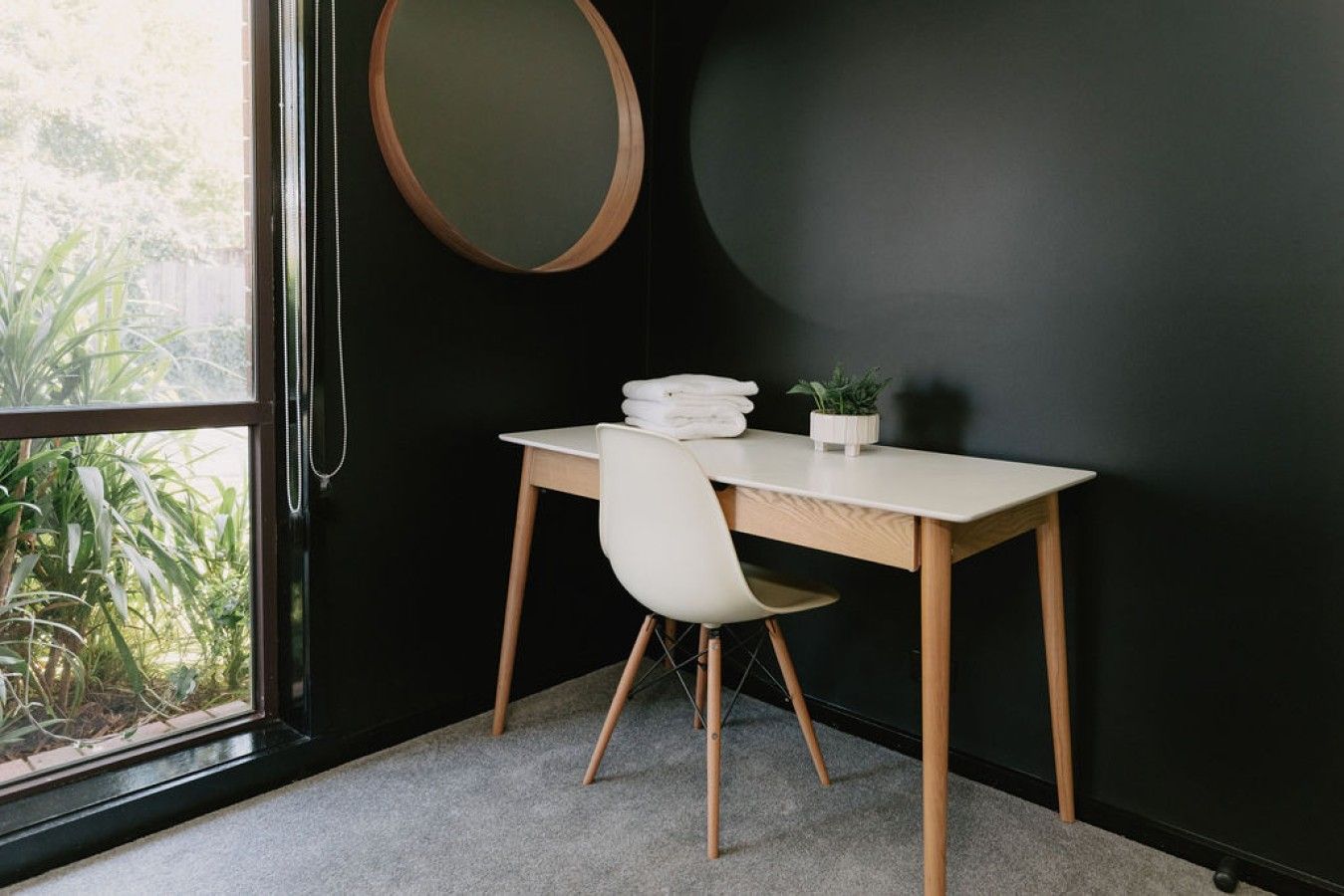 A room with a desk, chair, and a round mirror on the wall.