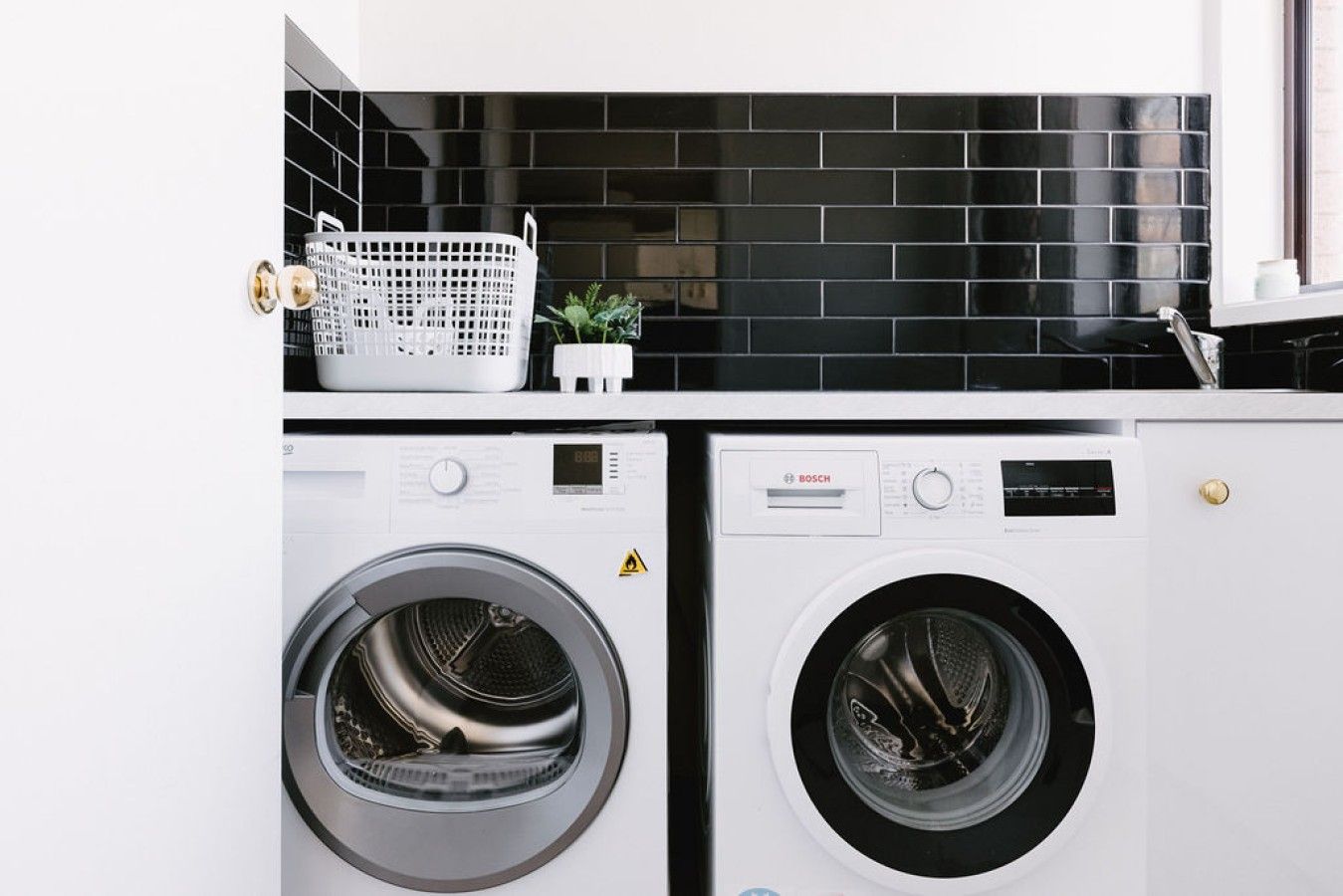 A laundry area with two front-loading washing machines and a black tiled backsplash.