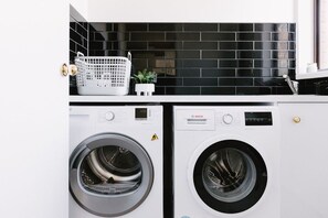 A laundry area with two front-loading washing machines and a black tiled backsplash.