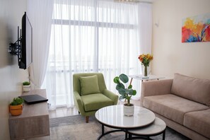 Una sala de estar moderna con un sillón verde, un sofá beige, una mesa de centro redonda y un televisor de pantalla plana montado en la pared.