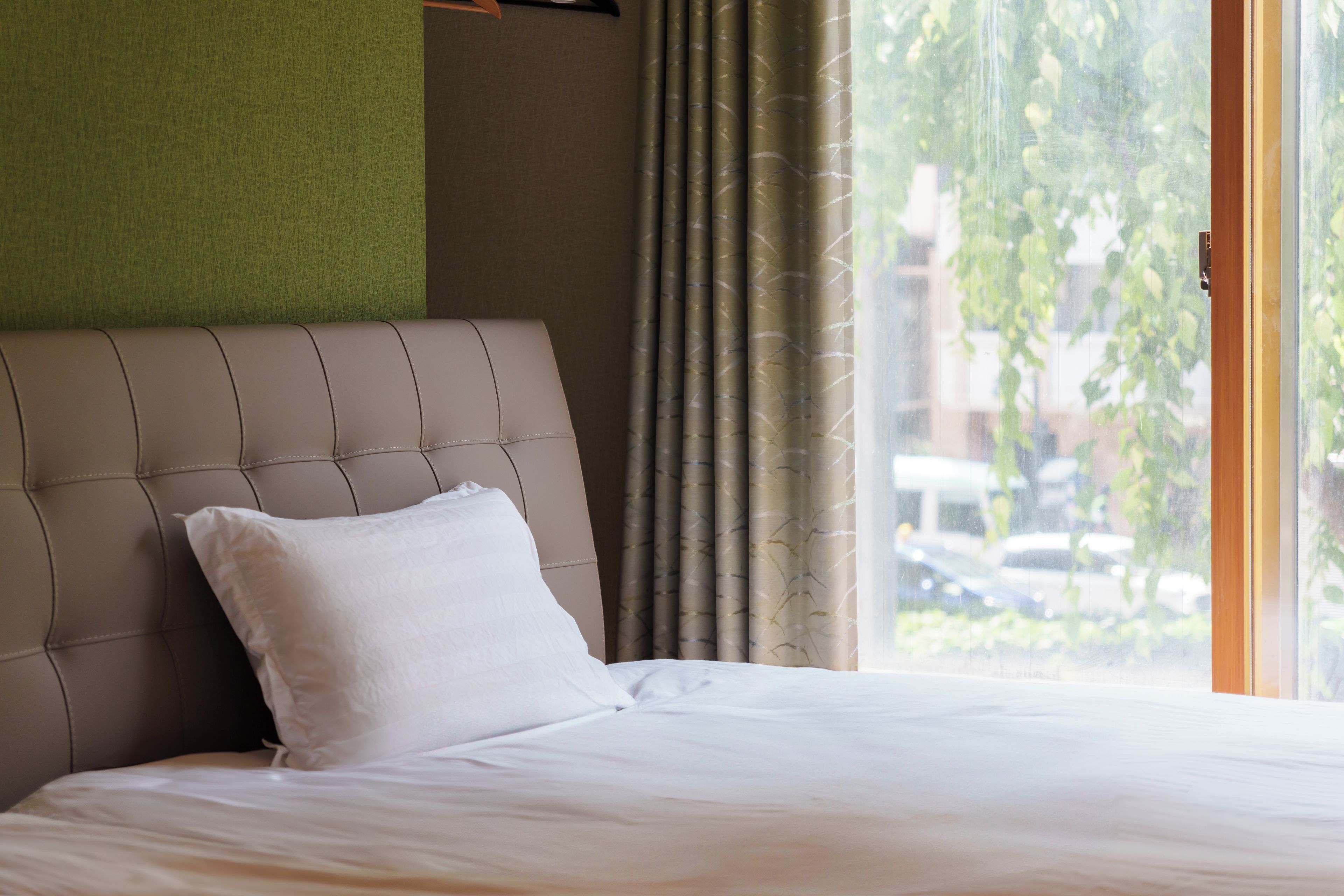 A hotel room with a bed, a headboard, and a window with curtains.