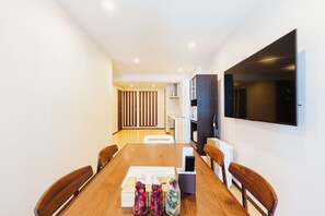 A modern dining area with a wooden table, chairs, and a large flat-screen TV mounted on the wall. - SERENE | Kuromon ・ 202 | 3BR ・ 2 Shower Rooms | Private Home for Families and Groups (Osaka)